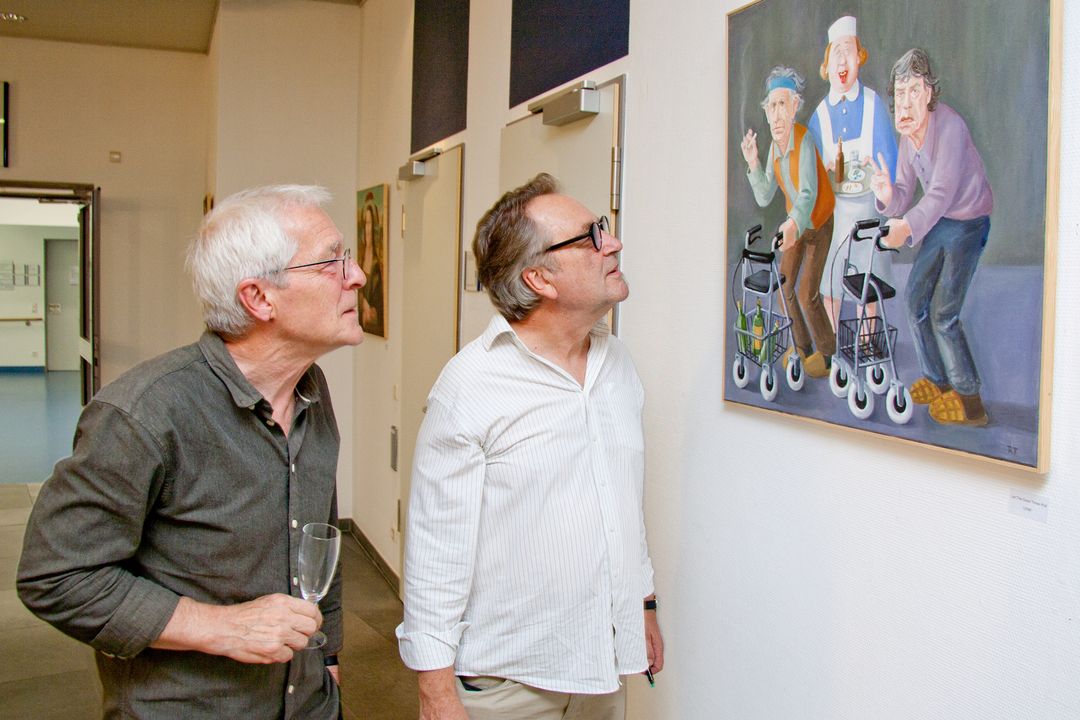 Zwei Männer sehen sich ein Bild an, auf dem die Rolling Stones als Rentner mit Rollatoren zu sehen sind.