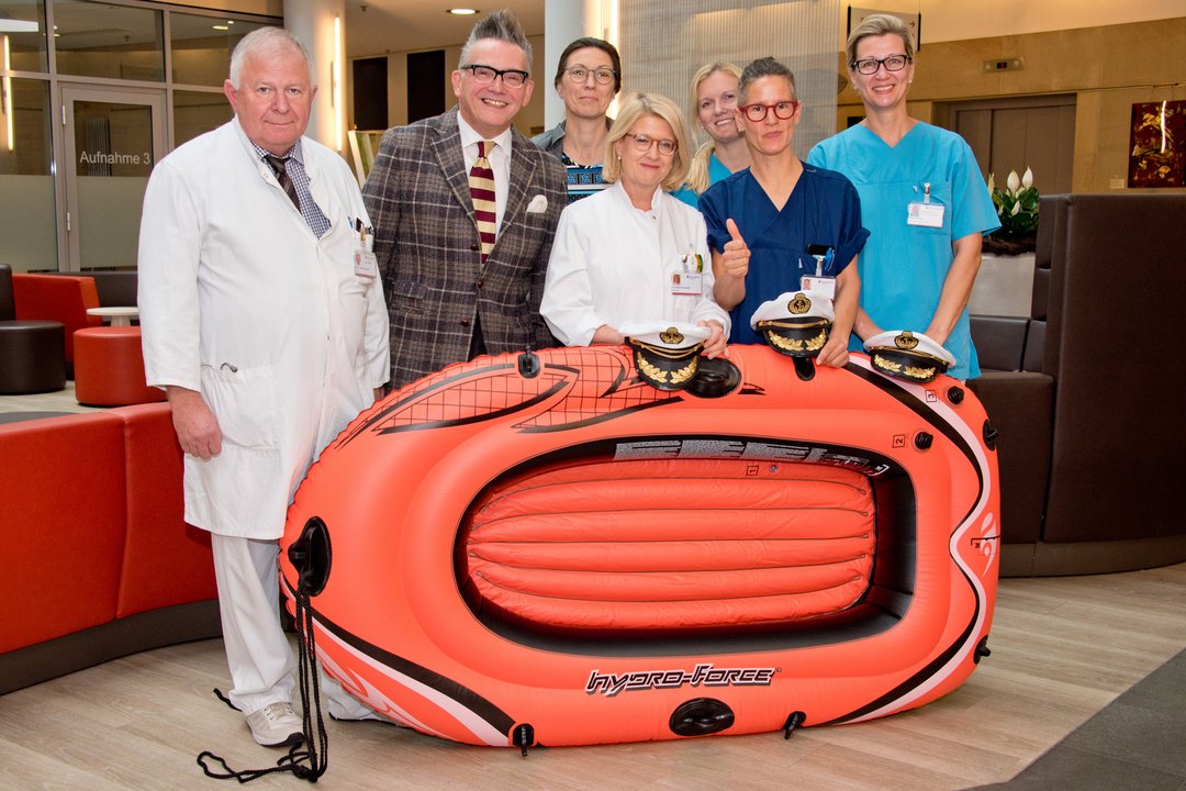 Götz Alsmann und mehrere Klinikmitarbeiter halten ein Schlauchboot.
