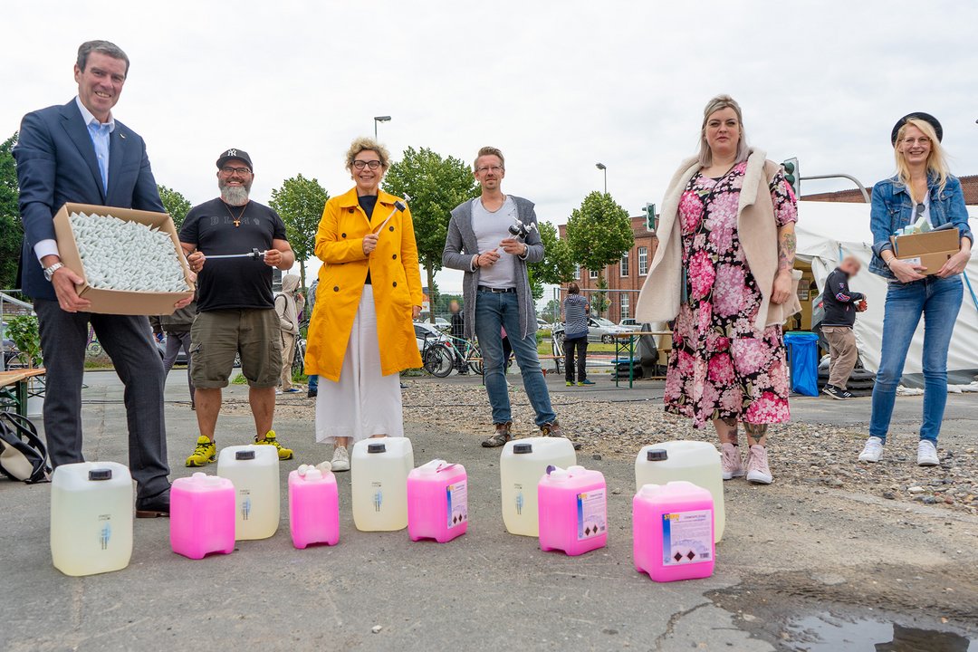 Mehrere Kanister stehen vor einer Gruppe von Menschen